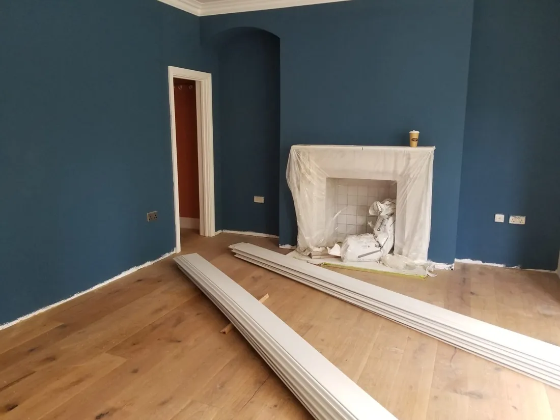 A principal room near completion — deep blue walls, engineered oak floor over the insulated structure, fireplace under protective sheeting